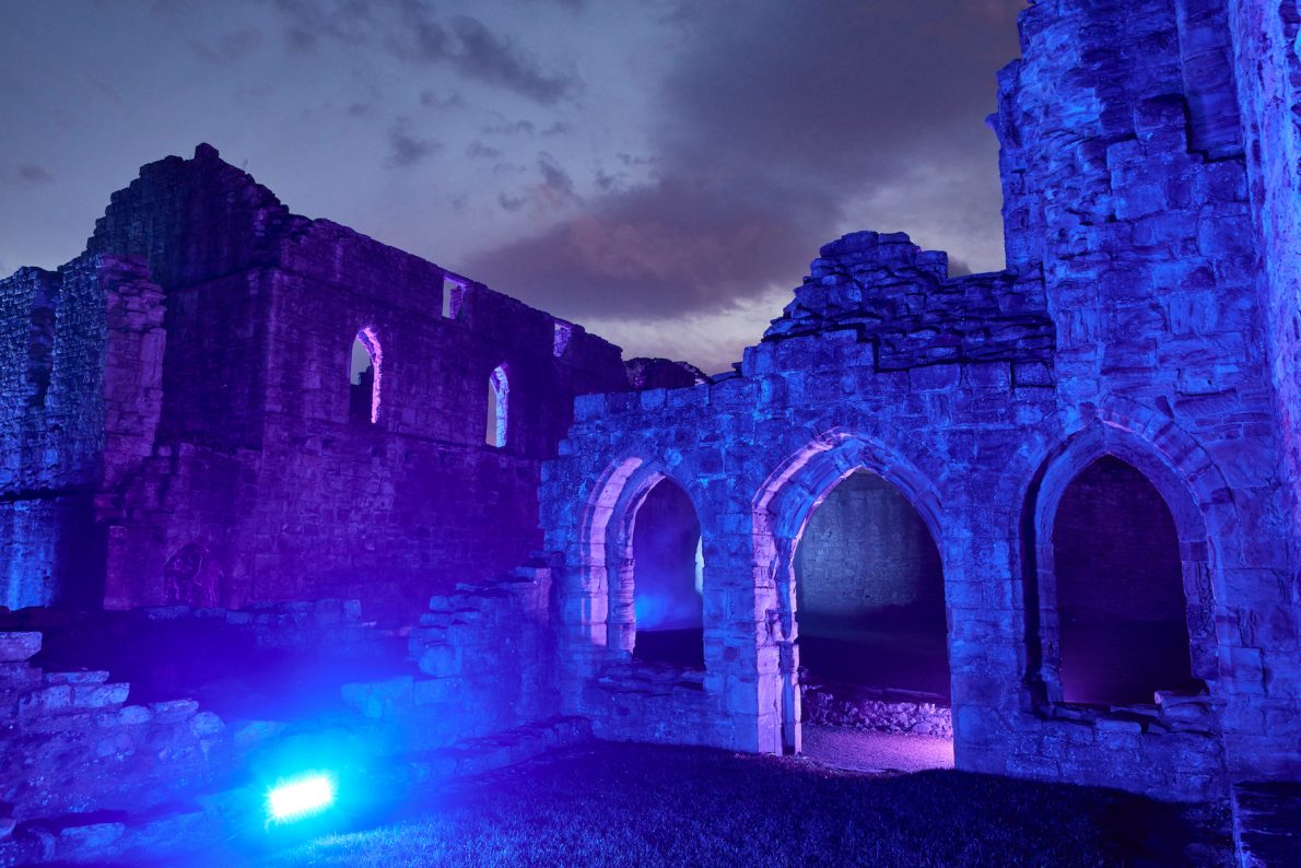 Finchale priory lit up with blue ambient light and smoke