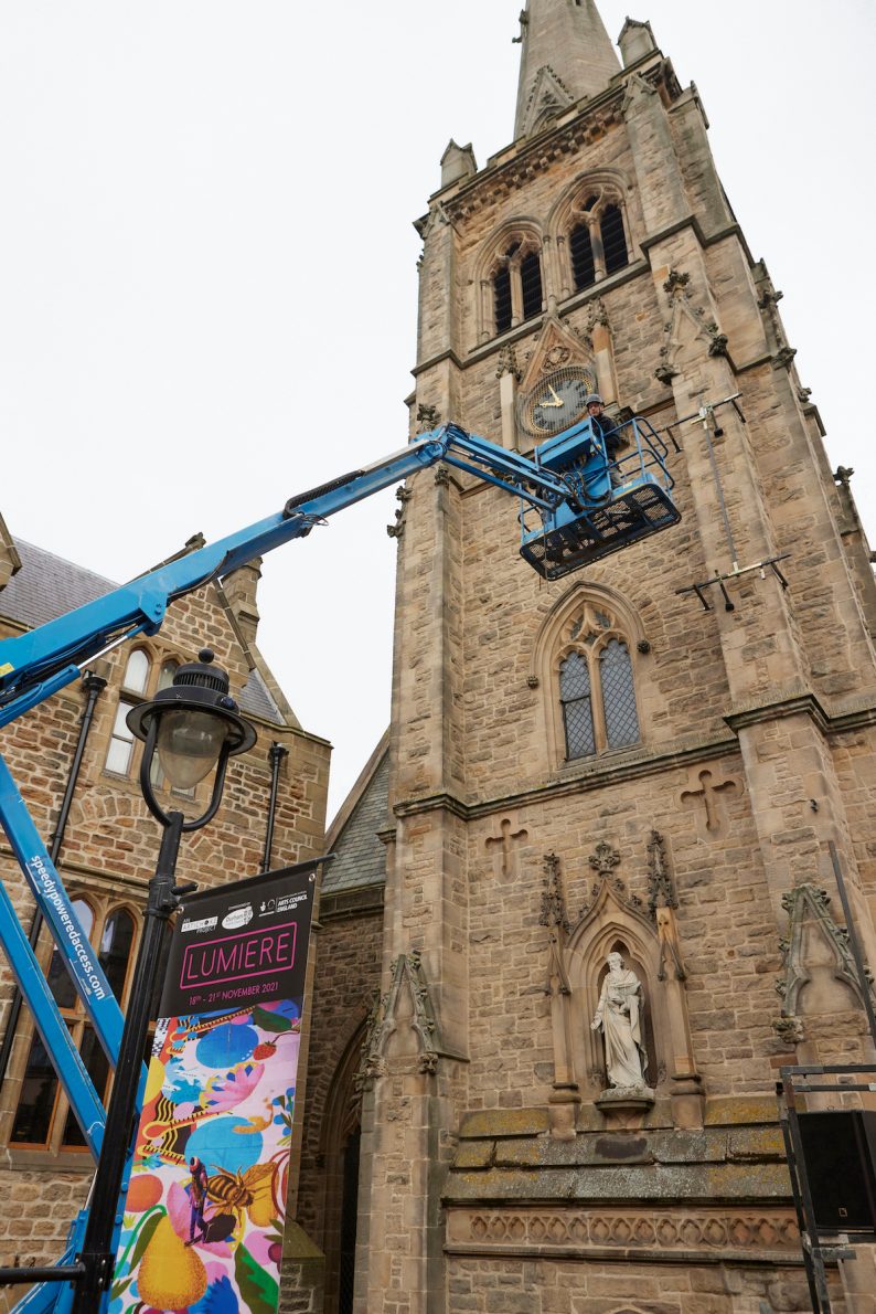 Man in a cherry picker putting up the Froggs on Durham Townhall