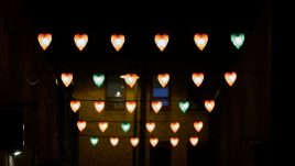 Rows of six lit up hearts hung up, in each row there is one green heart amongst the red ones