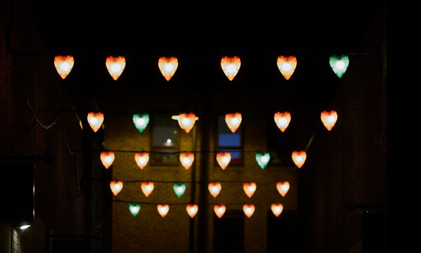 Rows of six lit up hearts hung up, in each row there is one green heart amongst the red ones