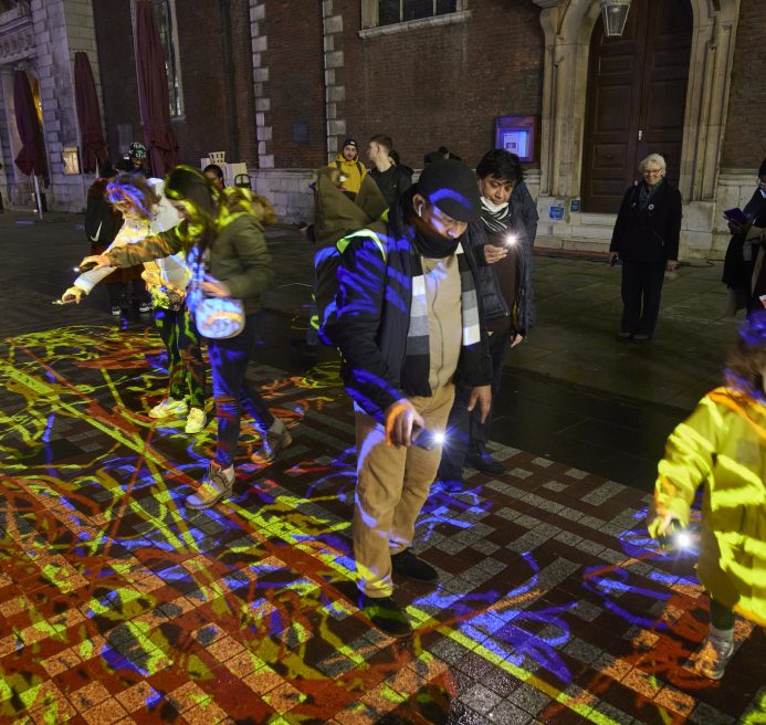 People interacting with a light installation where you draw with colourful lines on the ground using your phone torch