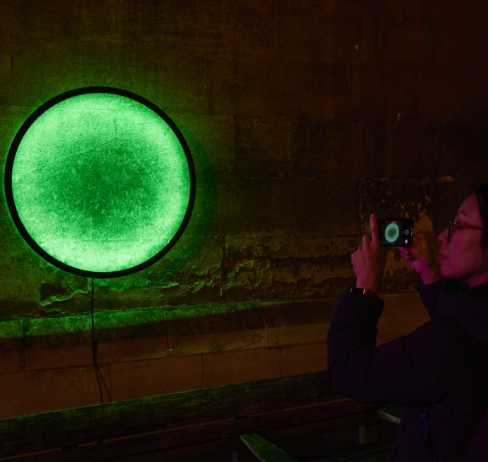 someone taking a photo of a circle on a wall creating an illusion of multicoloured portal