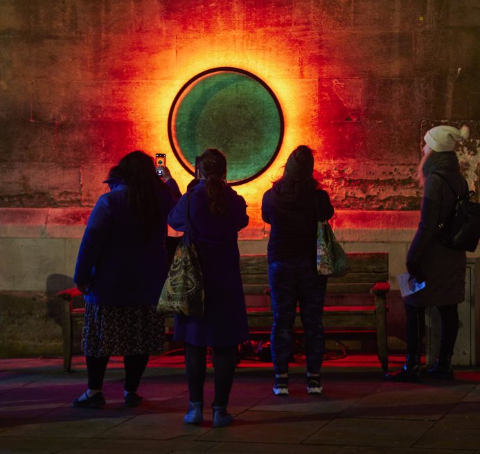 People in front of a circle on a wall creating an illusion of multicoloured portal