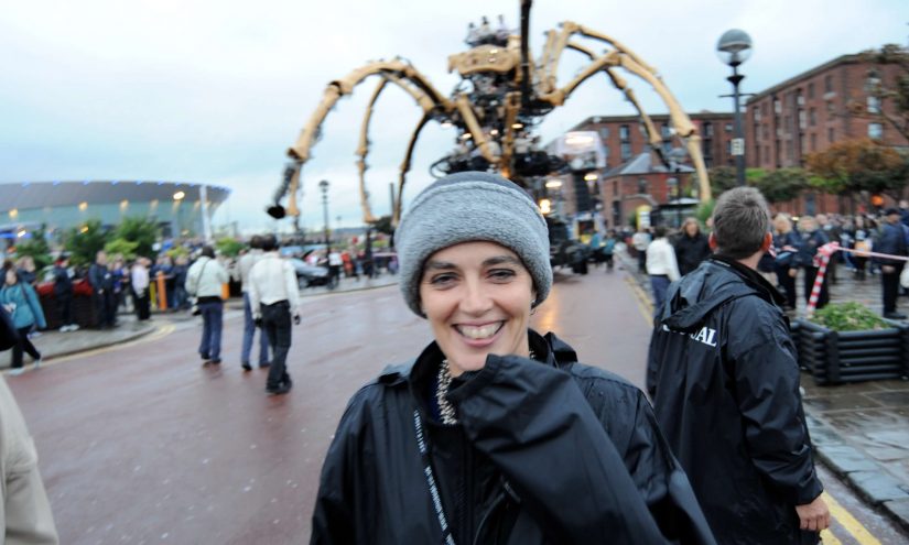 Artichoke's Director Helen Marriage wearing grey beanie hat standinf in front of La Machine - a huge mechanical spider structure in Liverpool
