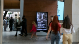 Photo of art by Martin Firrell on a digital screen. The image depicts a close up black and white photo of a commuter's crotch. The printed writing reads; 