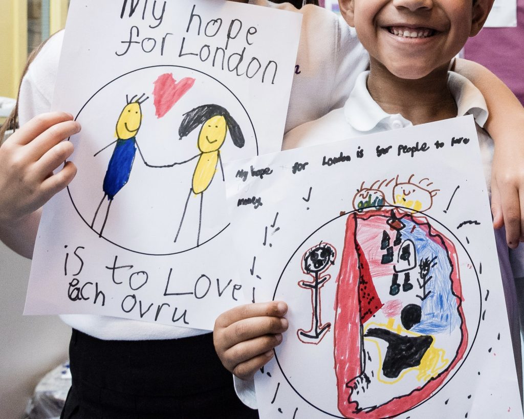 2 children holding drawings. One reads 'My hope for London is to love each ovru', the other reads 'my hope for London is for people to have money'.