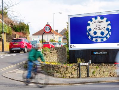 An image of a cake against a blue background on a billboard. The text, written in icing, on the cake reads: 'Let Them Eat Nothing'.