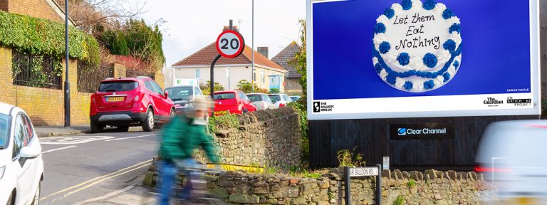 An image of a cake against a blue background on a billboard. The text, written in icing, on the cake reads: 'Let Them Eat Nothing'.