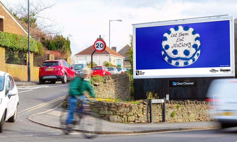 An image of a cake against a blue background on a billboard. The text, written in icing, on the cake reads: 'Let Them Eat Nothing'.