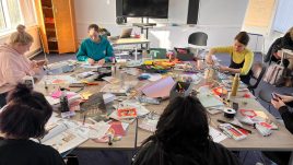 A workshop in Belfast for Season 2 of The Gallery. A group of young people sit in a room with piles of magazines on their work stations. They are creating collages in repsonse to the theme 