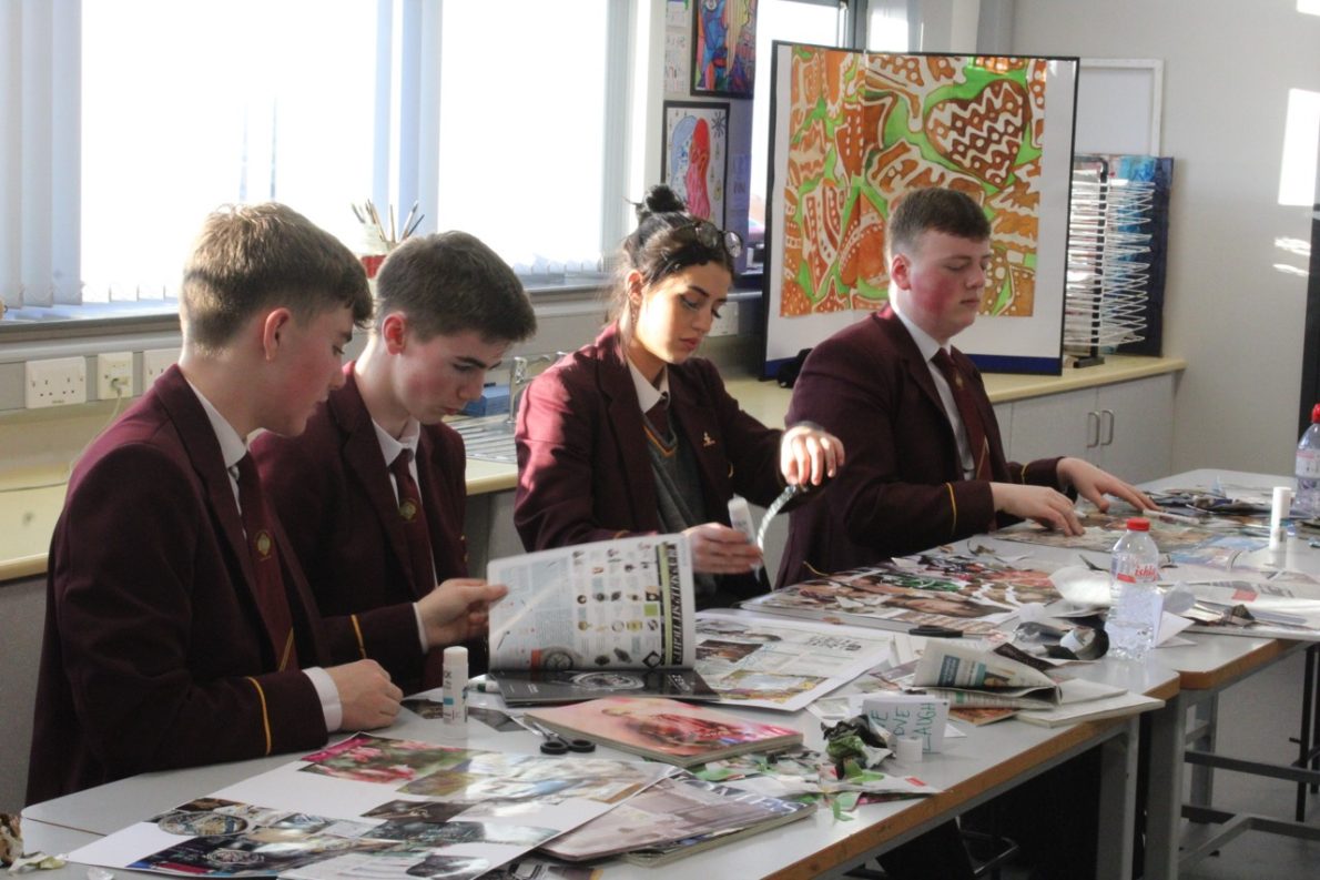 A photo from a schools workshop in Northern Ireland for Season 2 of The Gallery. A group of young people sit in a classroom with piles of magazines on their work stations. They are creating collages in repsonse to the theme 