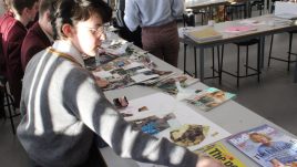 A photo from a schools workshop in Northern Ireland for Season 2 of The Gallery. A group of young people sit in a classroom with piles of magazines on their work stations. They are creating collages in repsonse to the theme 