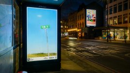 A bus shelter screen of the artwork ‘CRY’ (2022) by Allyson Packer on a busy London road at night. A barren landscape. A freight train can barely be seen in the distance. A road sign in the foreground reads 'CR Y'.