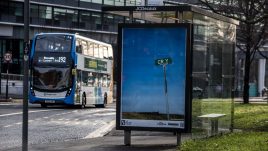 A bus shelter screen of the artwork ‘CRY’ (2022) by Allyson Packer in Manchester. A barren landscape. A freight train can barely be seen in the distance. A road sign in the foreground reads 'CR Y'.