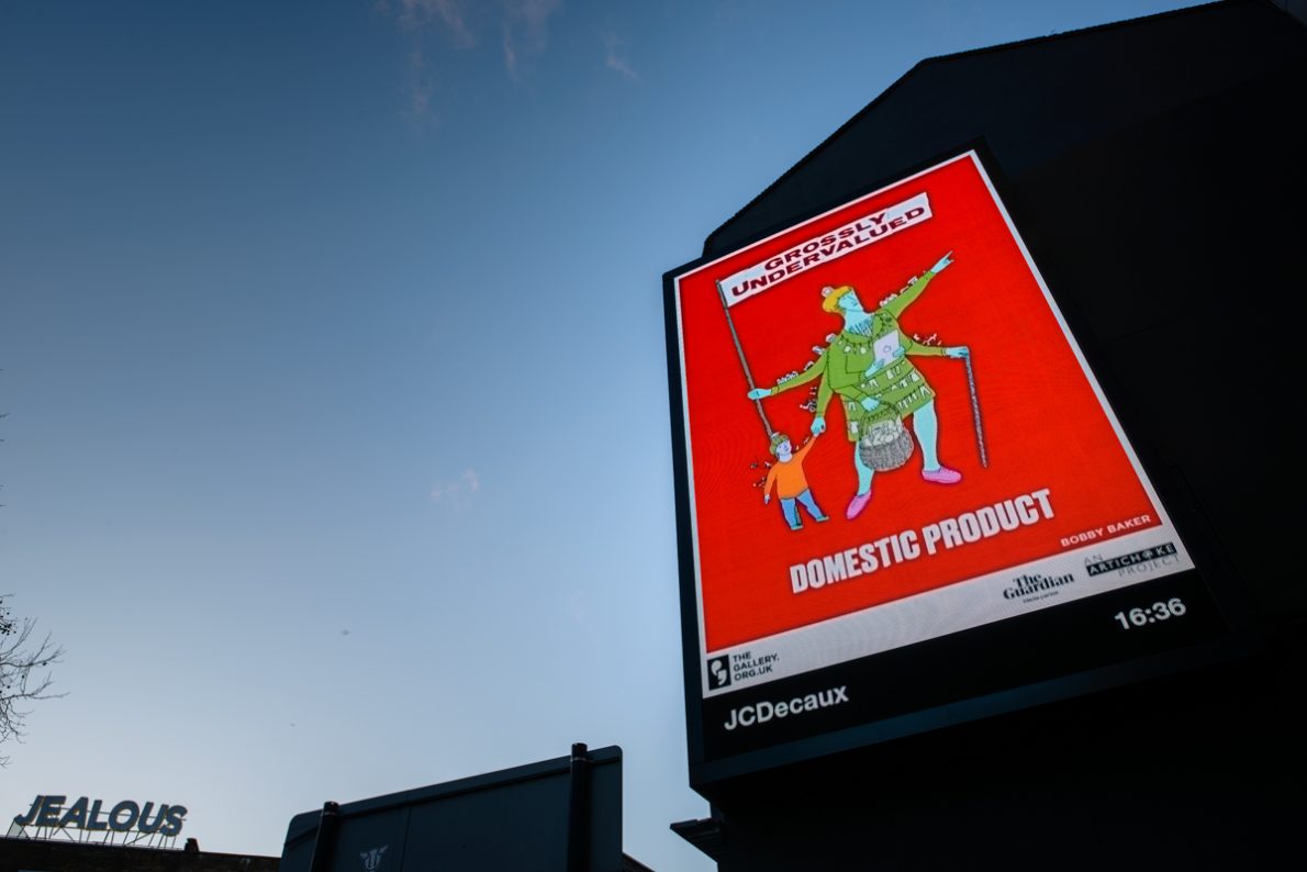 A billboard of the artwork ‘GROSSLY UNDERVALUED DOMESTIC PRODUCT’ (2022) by Bobby Baker against a sunset. A colourful sketched character on a red background. The central figure is adorned with cooking utensils, washing and other domestic symbols. She has several arms; one holds a bulging shopping basket and another arm leans on a walking cane. A child's hand tightly grasps onto another hand and one arm holds a large flag with text across it. The text reads: 'GROSSLY UNDERVALUED DOMESTIC PRODUCT'.