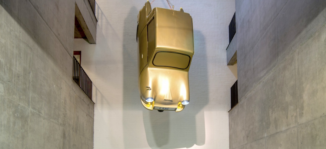 A gold car suspended in a gallery