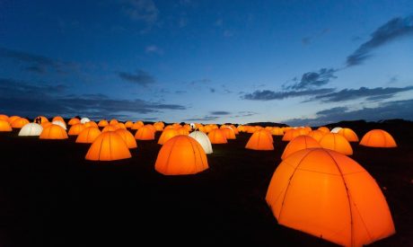 Tents seen at dusk. They are lit up bright orange.