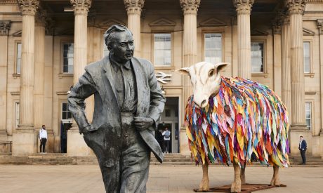 Aina, the Mother Sheep Sculpture, in front of St George’s Square. The statue of Harold Wilson is in the foreground and the station is in the background.