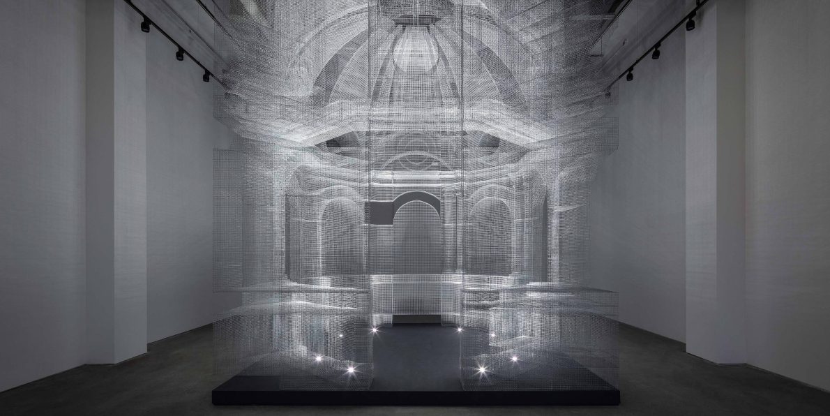 A ghostly render of a cathedral building in a spacious room. The installation is made with wire mesh and illuminated from within.