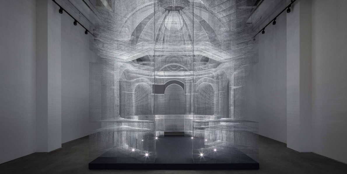 A ghostly render of a cathedral building in a spacious room. The installation is made with wire mesh and illuminated from within.