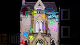 The artwork 'Colourful Chaos', Emma Allen. Outside Durham's Masonic Hall at night. A stop motion short film is projected onto the exterior. Colourful clay teddy bears climb across and paint the brickwork.